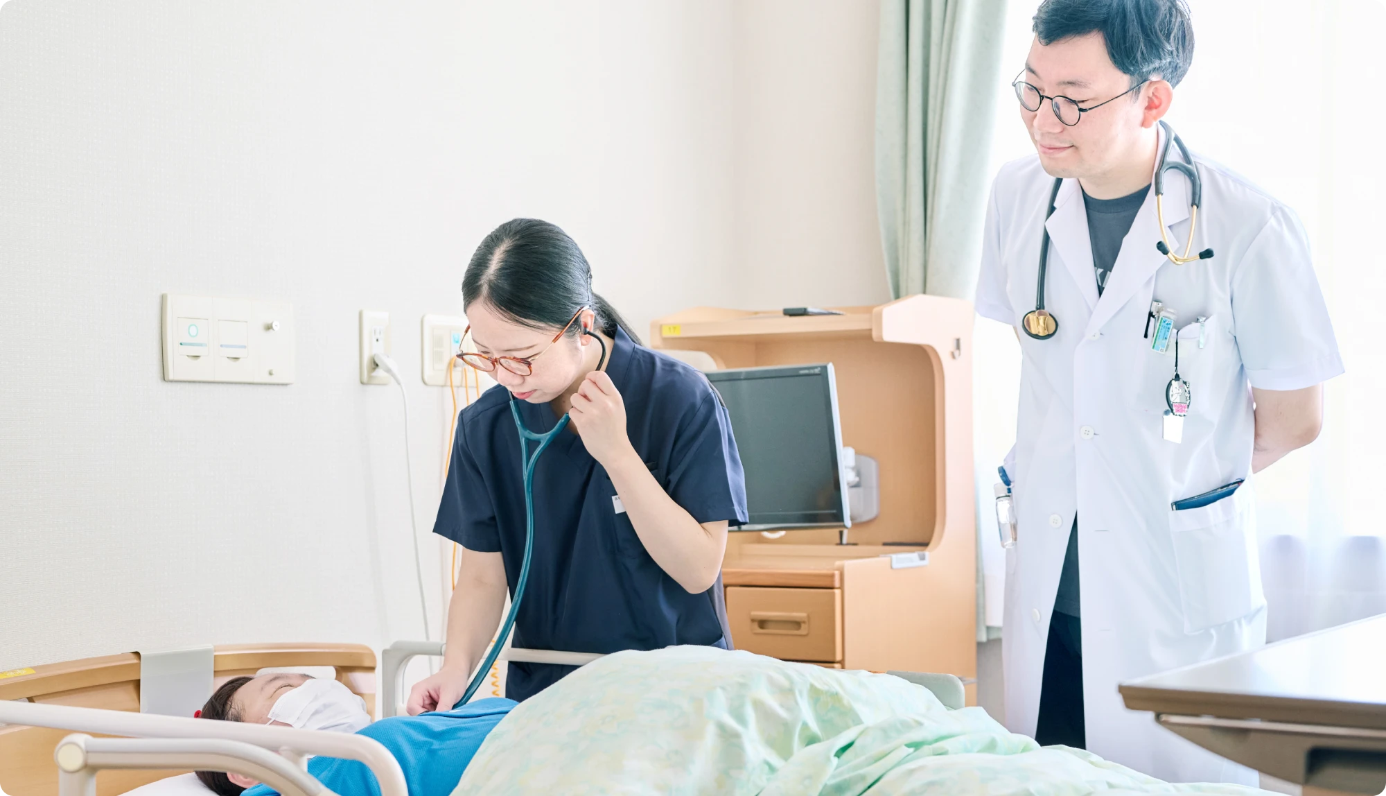 病室で患者を診察する医師と研修医